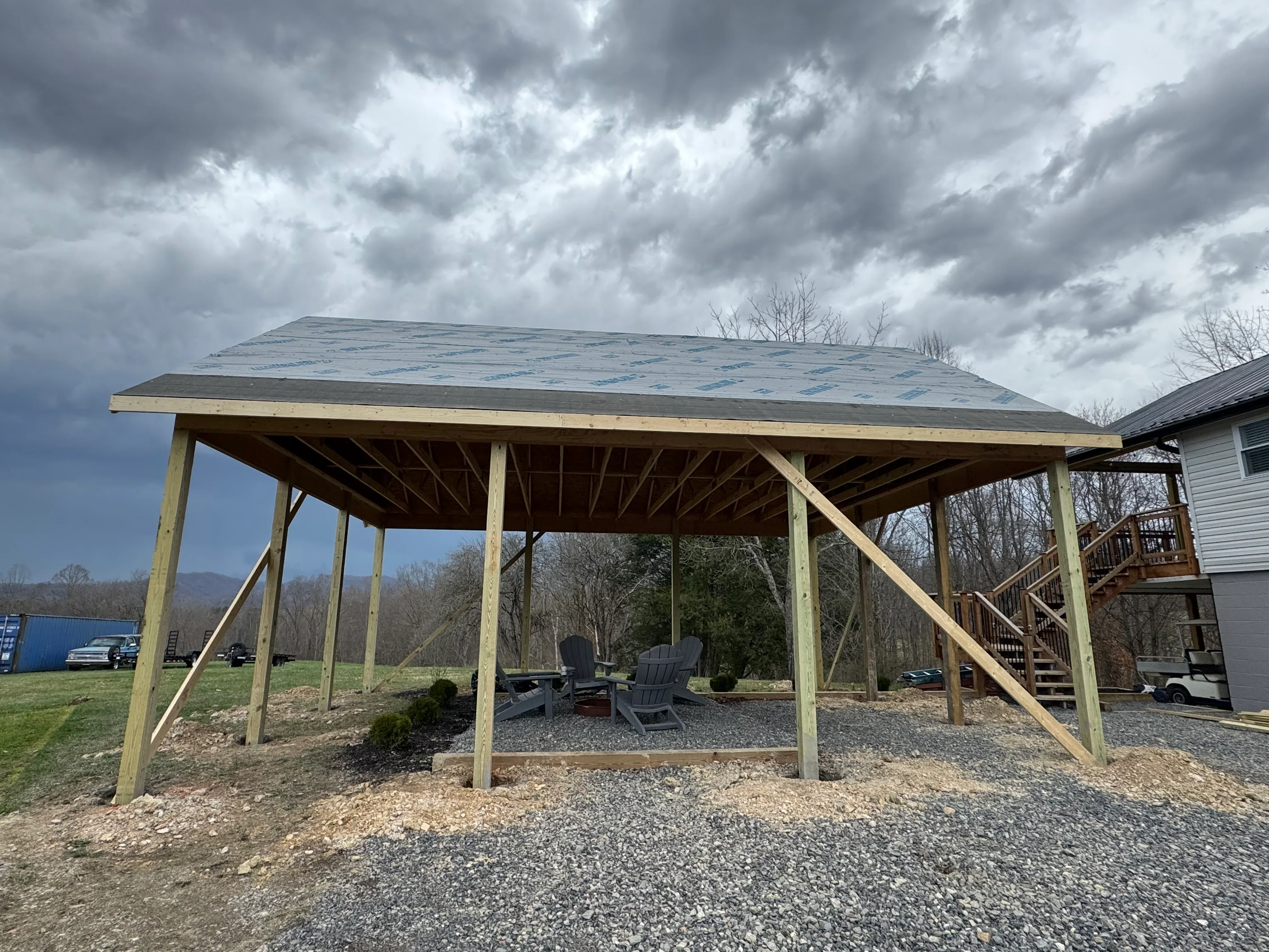 Wooden pavilion with metal pitched roof, timber posts, and diagonal bracing over gravel patio